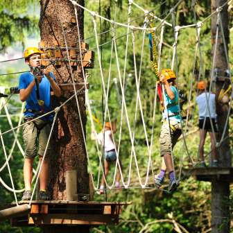 Kinder und Jugendliche mit Helmen im Hochseilgarten des Seilparks Triesen in Liechtenstein, gesichert auf Kletterelementen im Wald