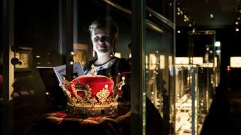 Junge Frau betrachtet eine prunkvolle Krone hinter Glas im Liechtensteinischen Landesmuseum.