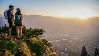 Tina Weirather und Marco Büchel stehen auf einem Berggipfel und blicken bei Sonnenuntergang über das Rheintal in Liechtenstein